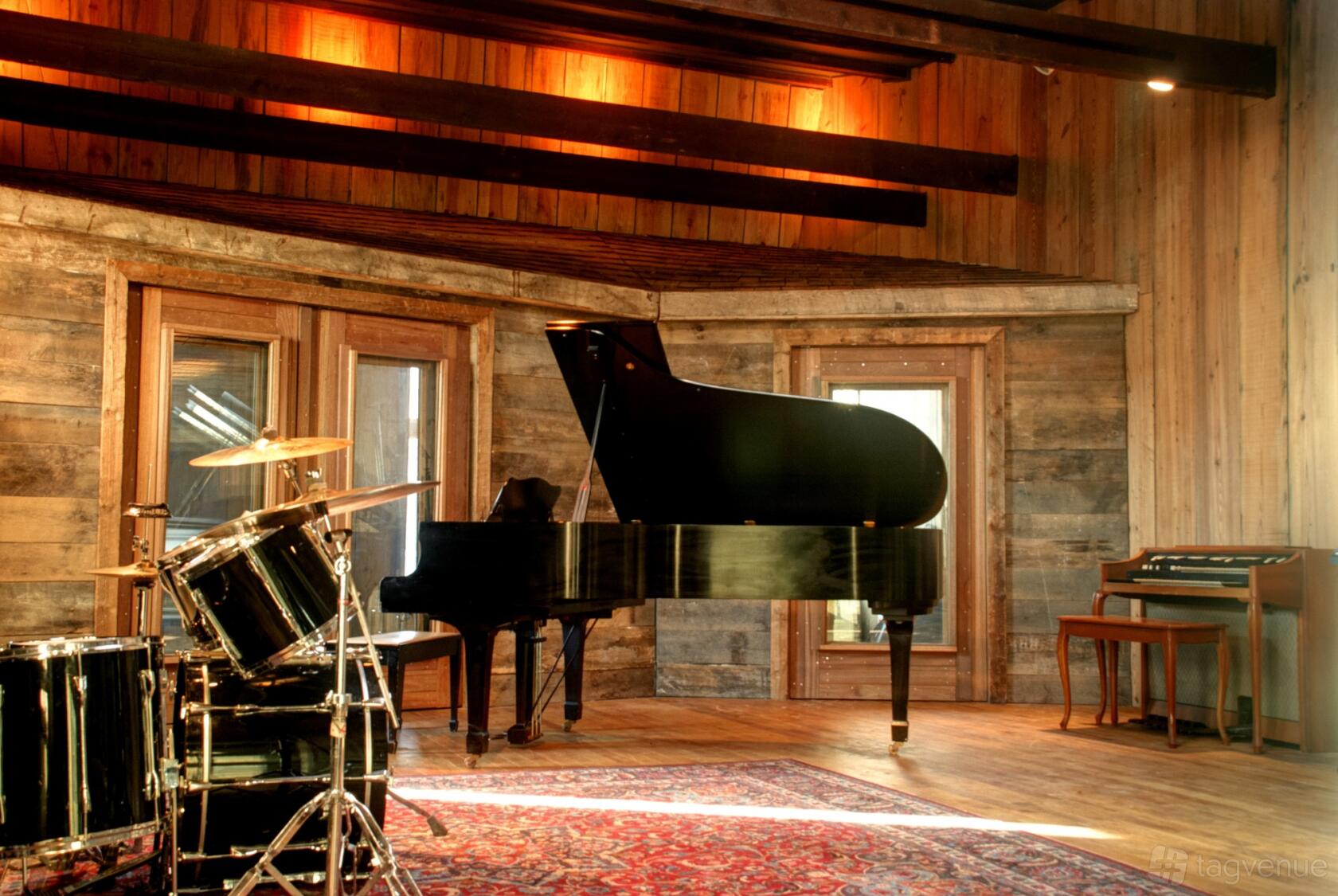 A recording studio with a grand piano, drum kit, wood paneling, and a patterned rug at Atomic Sound LLC.