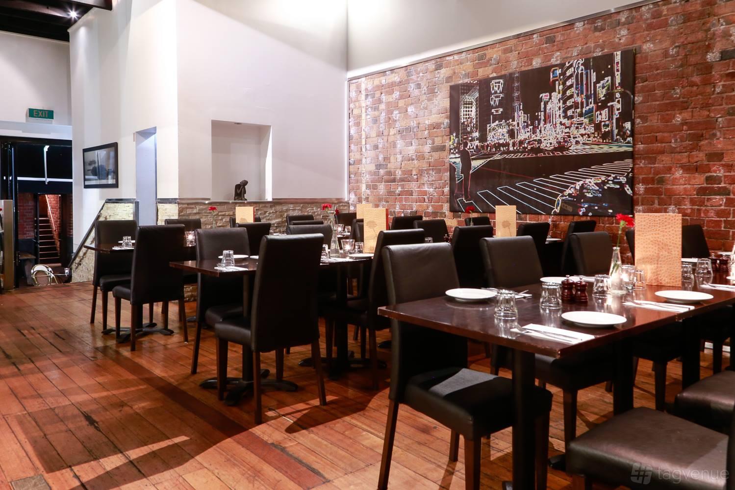 An event space in a restaurant with exposed brick walls, wooden floors, and black chairs at Grill Steak Seafood.