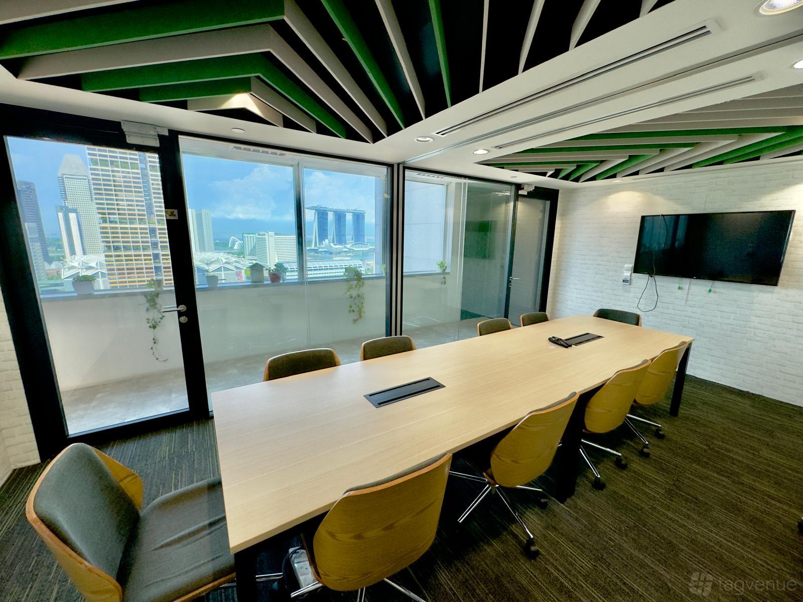 A meeting room with a long conference table, wall-mounted screen, glass doors, and city views at O2 Work @ Odeon Towers.
