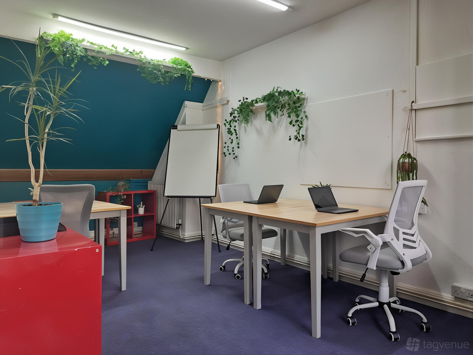 A coworking space with potted plants, ergonomic chairs, laptops, and a flip chart at The Hub on the Green.