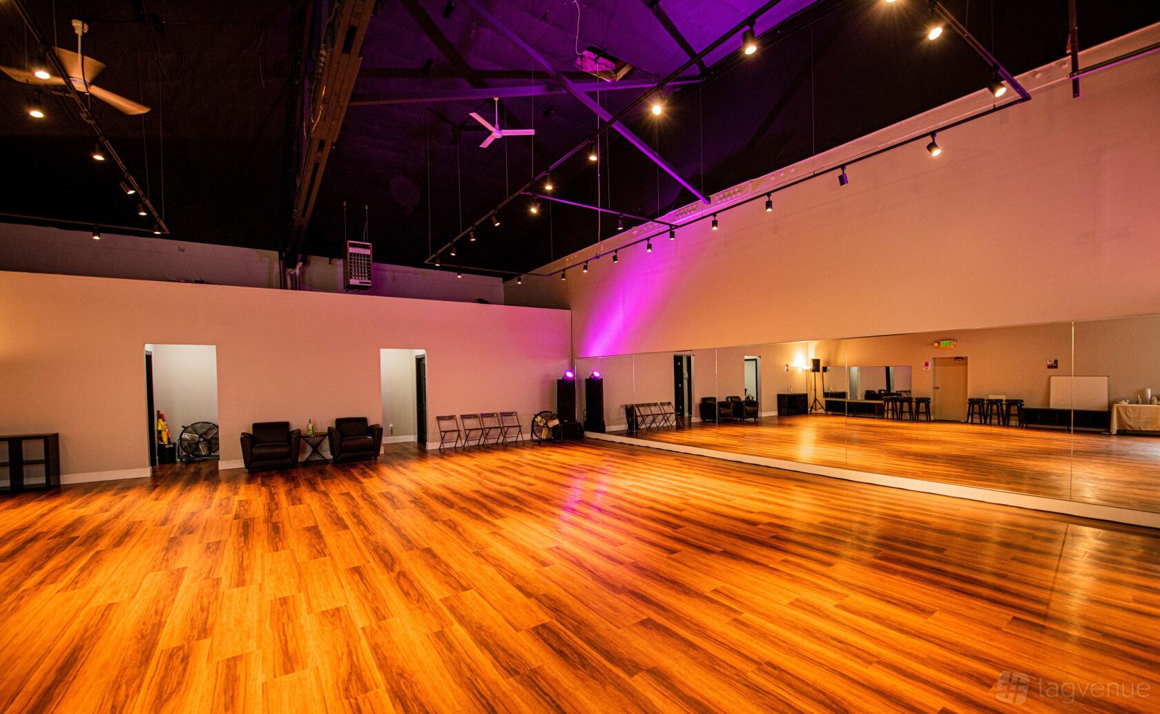 A dance studio with polished wood floors, full wall mirrors, lounge chairs, and uplighting at Baila District.