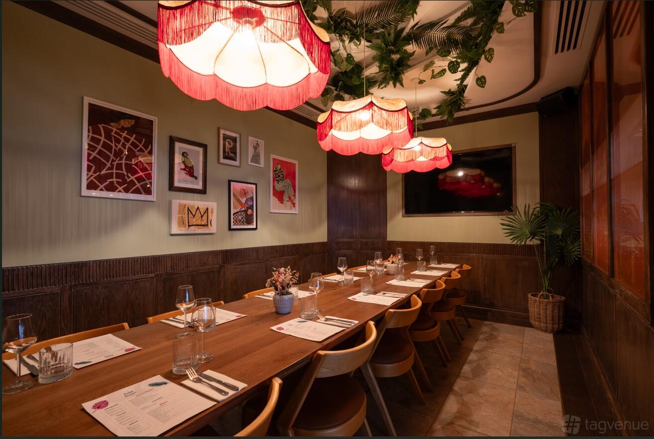 A private dining room with a long wooden table, pendant lights, framed artwork, and lush greenery at The Palm House.
