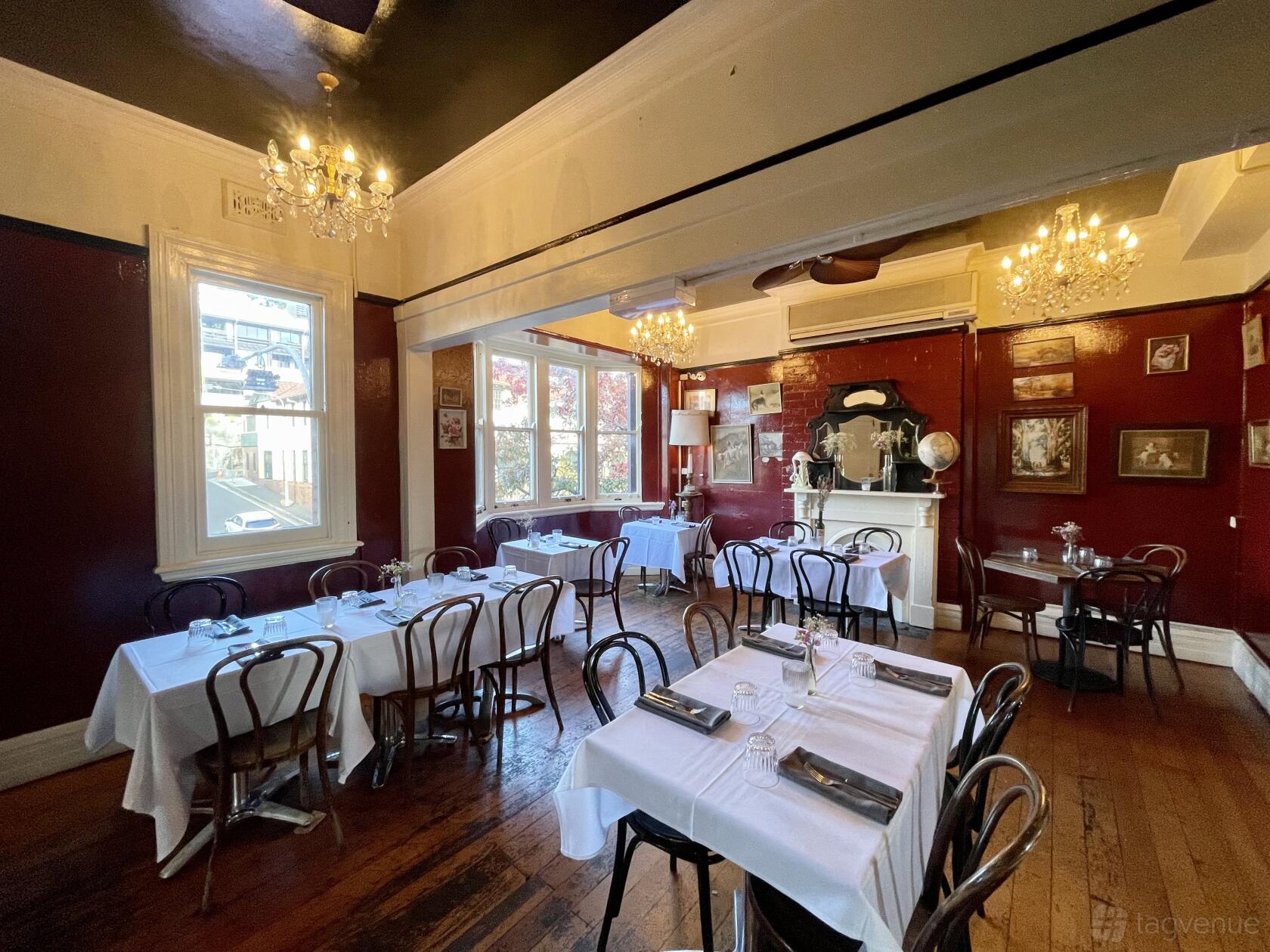 An event space in a pub with dark red walls, chandeliers, and round tables with white linens at The Old Fitzroy Hotel.