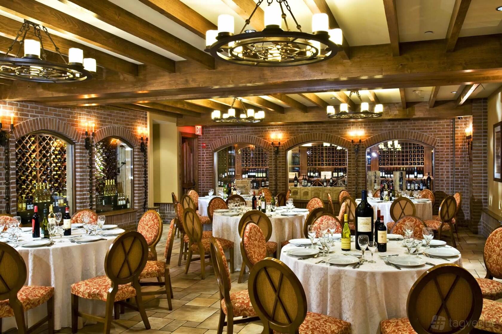 A dining room with exposed brick walls, wine racks, and round tables with white linens at Vetro Restaurant & Lounge.