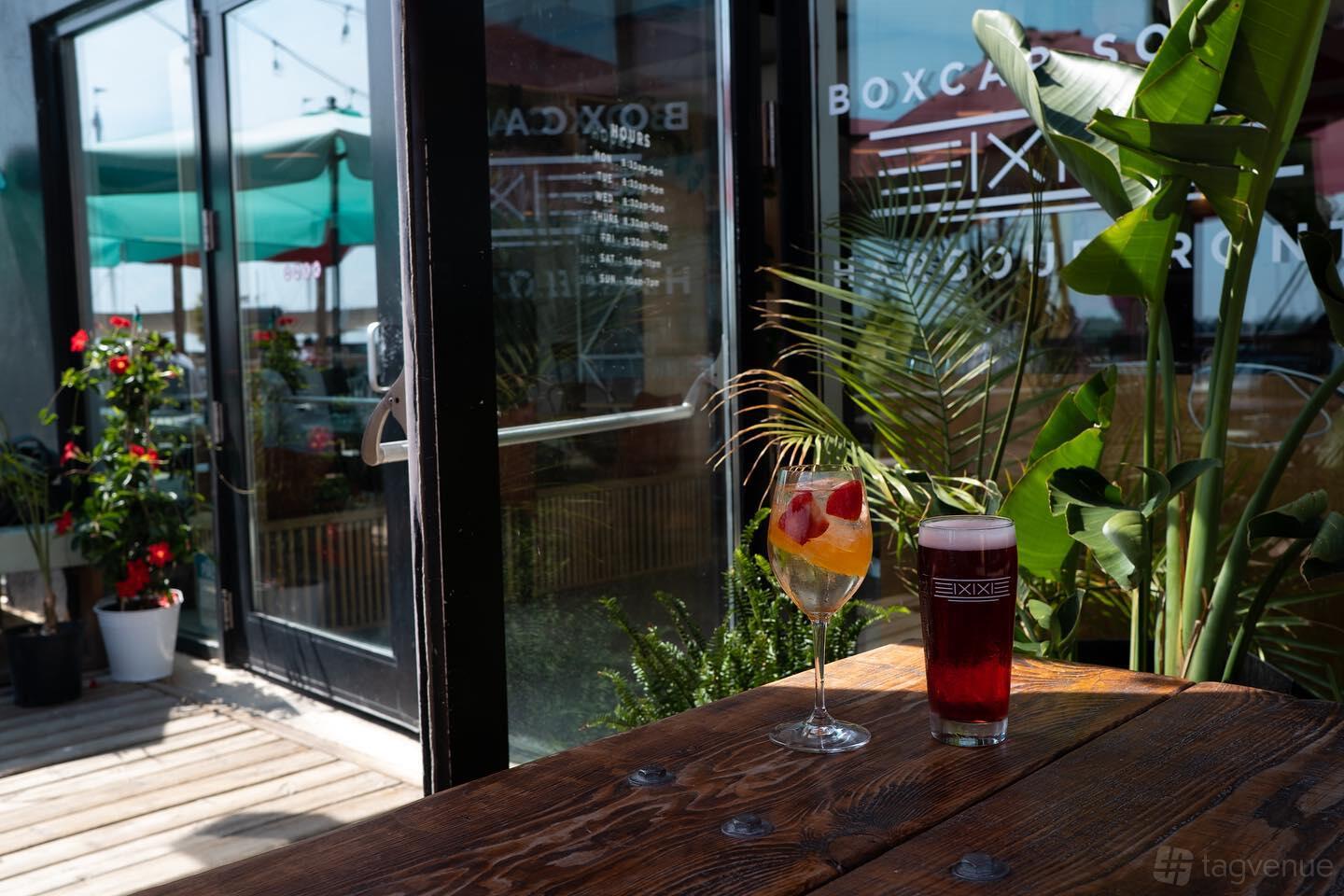 A café patio with potted plants, wooden tables, and drinks served outdoors at Boxcar Social - Harbourfront.