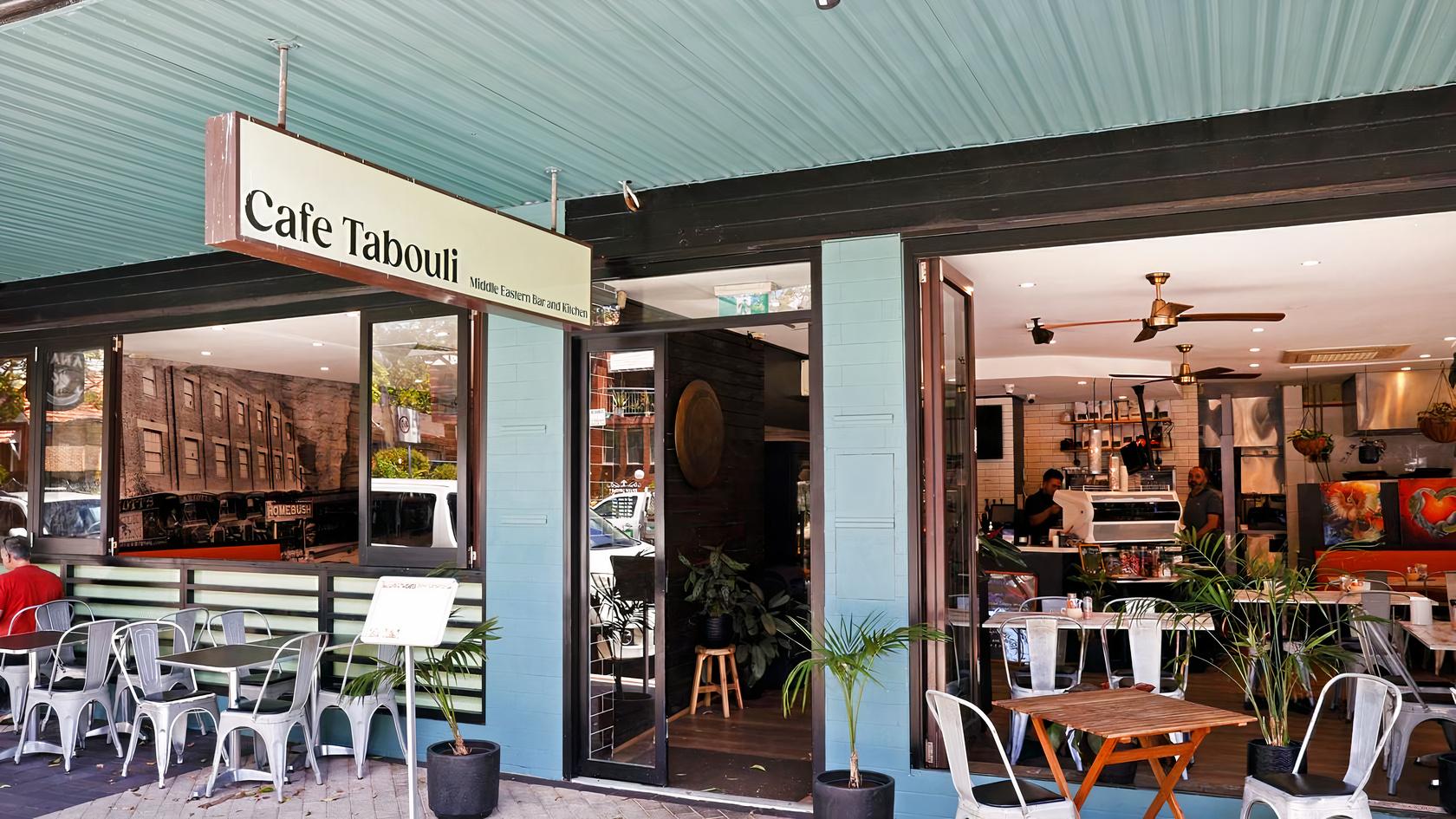 A café with outdoor seating, potted plants, and a large open entrance at Cafe Tabouli.