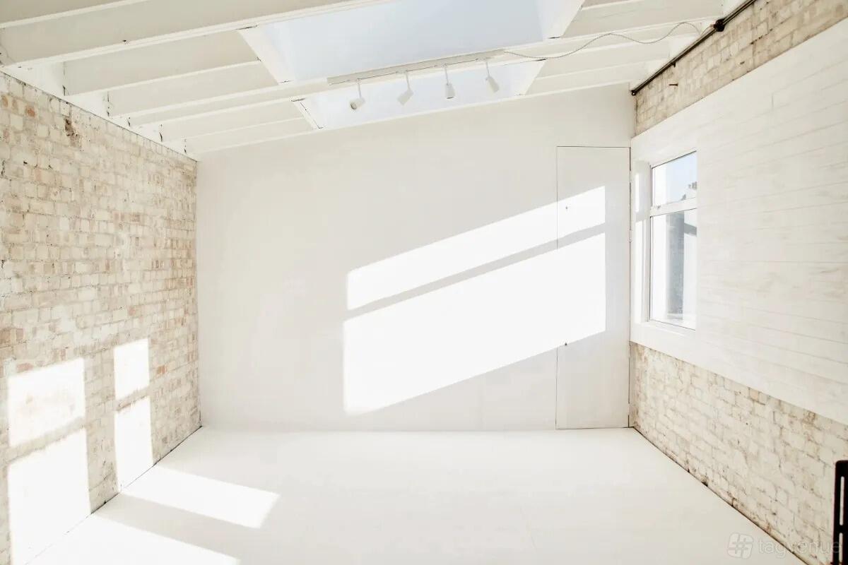 A photo studio with exposed brick walls, white floors, and a skylight providing natural light at Stepthirtyone.