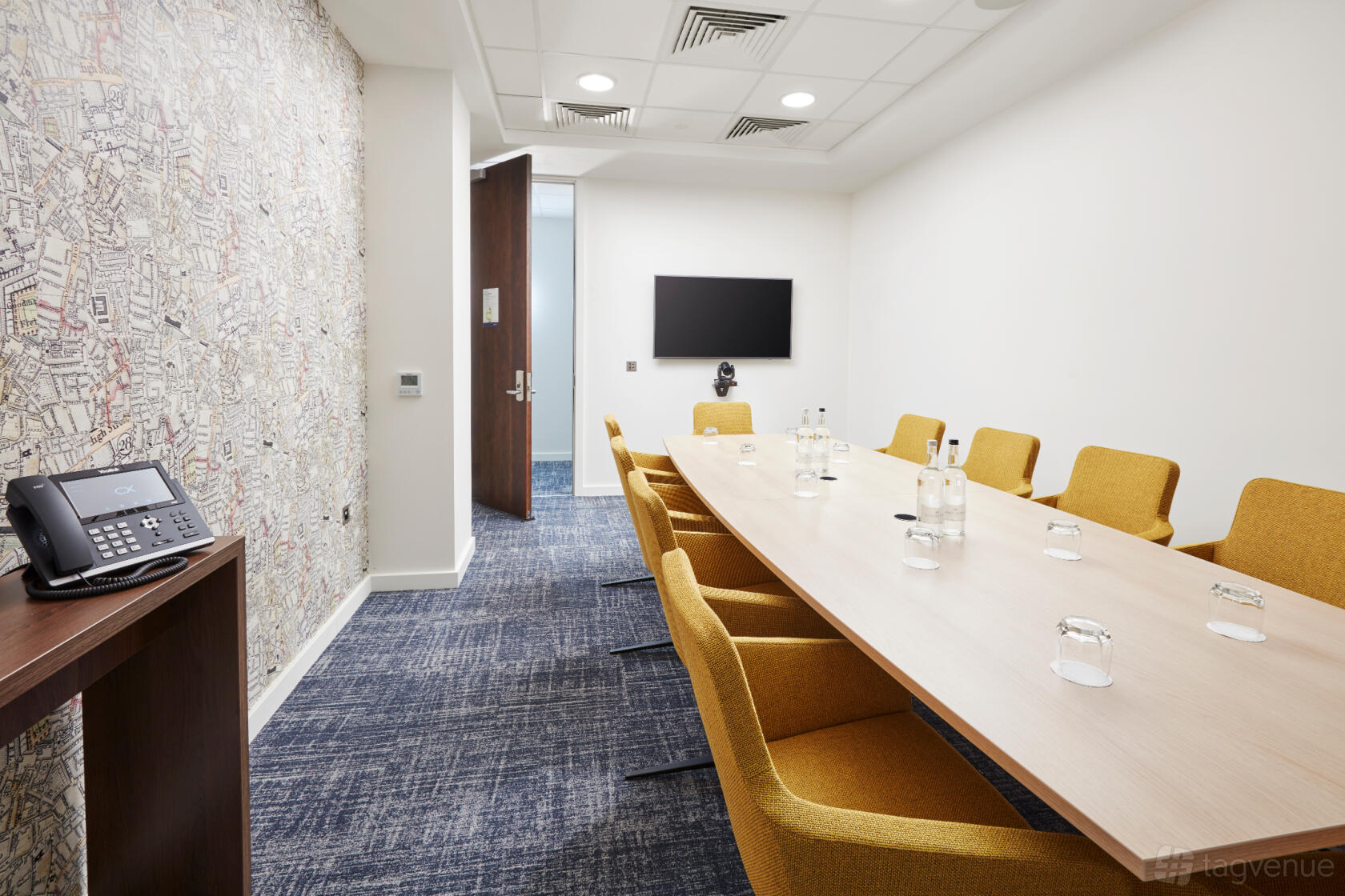 A meeting room with a long wooden table, mustard chairs, a map accent wall, and wall-mounted screen at Marlin Waterloo.