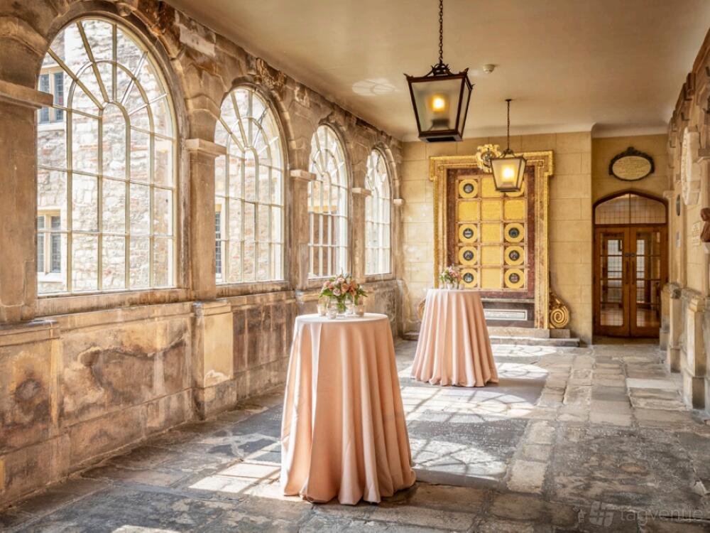 A museum cloister with arched windows, stone flooring, and high round tables with pink linens at The Charterhouse.