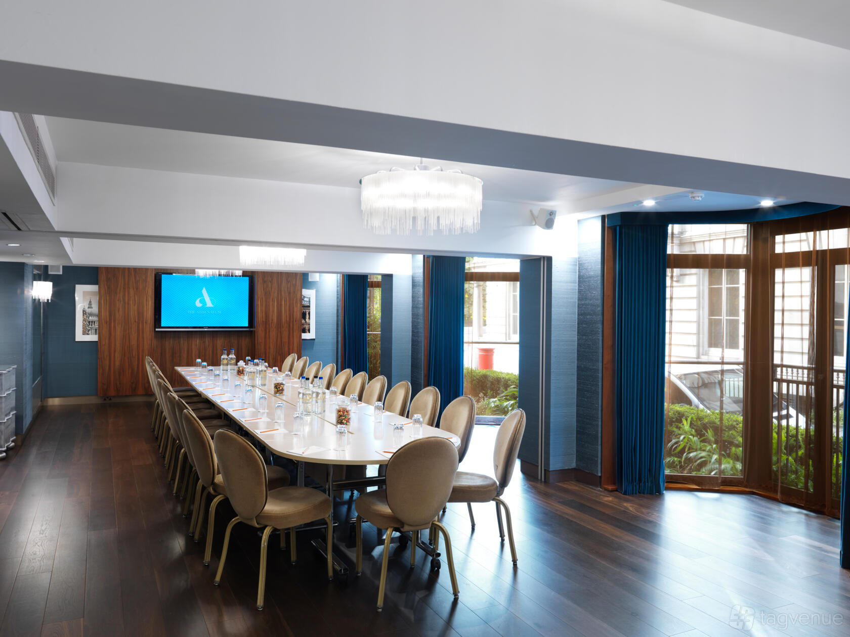 An event space with a long polished table, upholstered chairs, wood floors, and large windows at The Athenaeum Hotel & Residences.