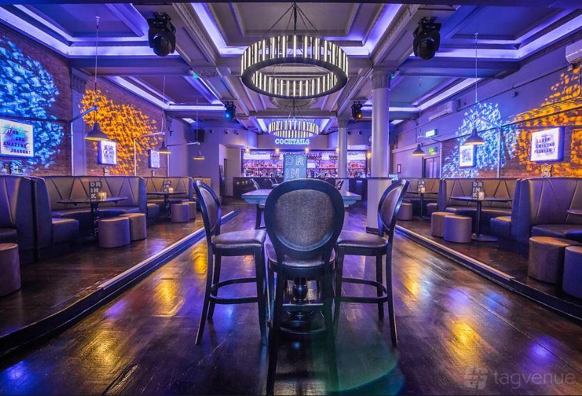 An event space in a bar with booth seating, colorful accent lighting, and circular chandeliers at Sway.