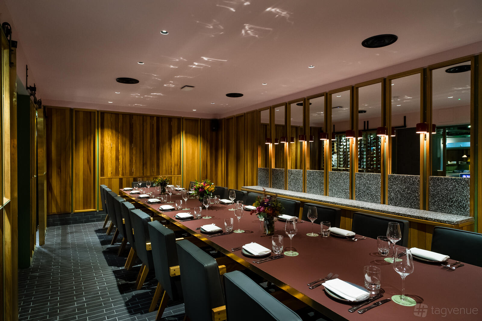A dining room with a long burgundy table, black chairs, wood-paneled walls, and mirrored accents at temper Soho.