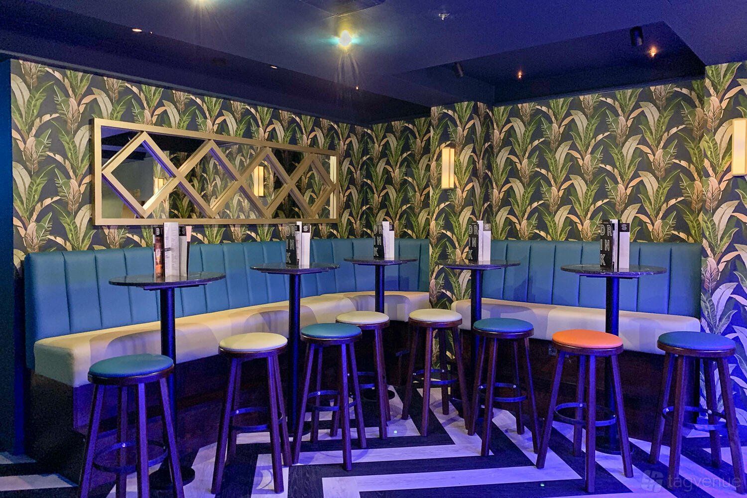 An event space in a bar with patterned wallpaper, blue banquette seating, and high tables with colorful stools at Sway.