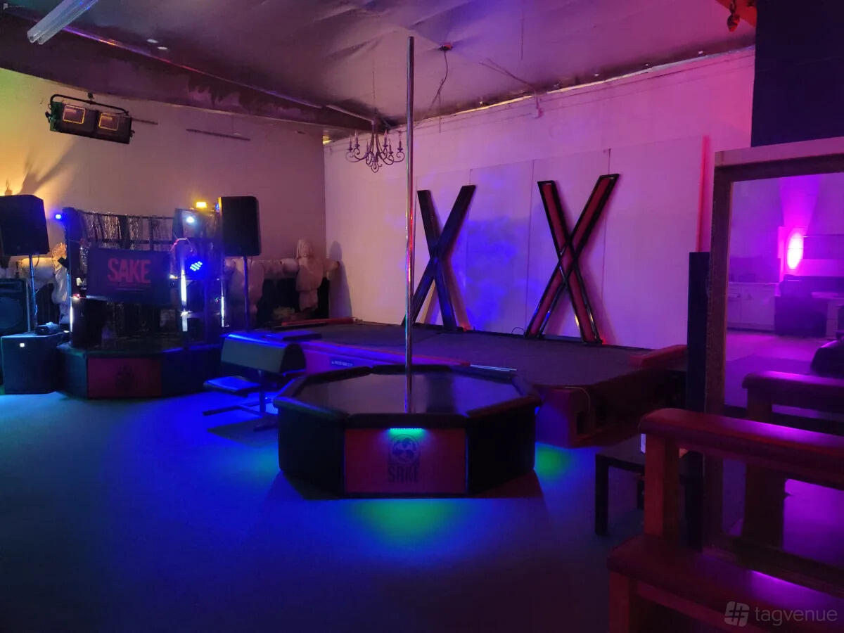 A photo studio with a stage, pole, BDSM equipment, and colored accent lighting at Cosmic Cube Creative Studio.