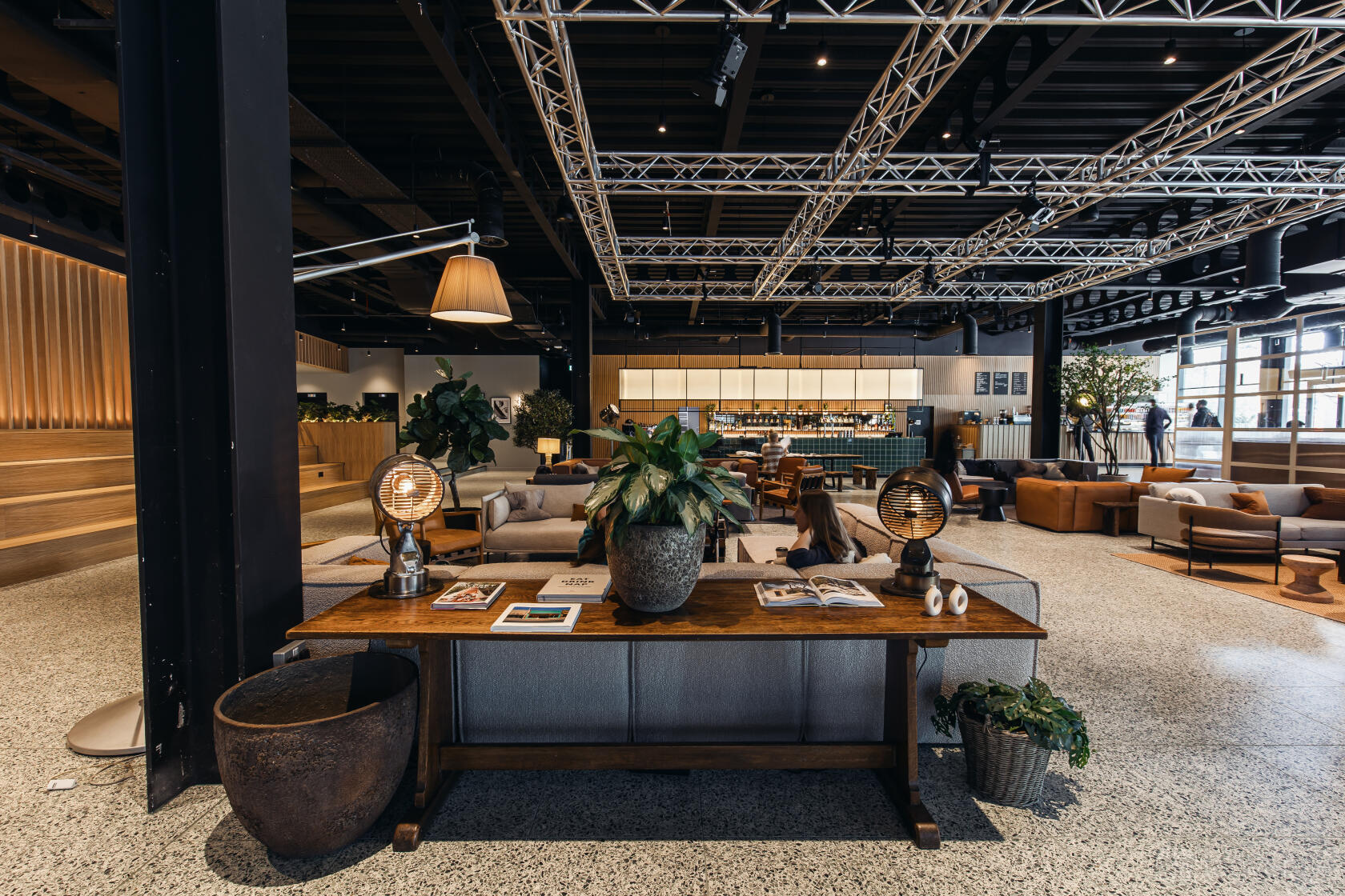 A lounge with a wooden table topped with lamps and plants, open seating, and visible bar at Fearns Leeds Dock.