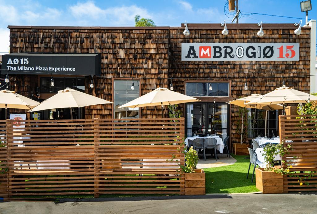 A restaurant with outdoor patio seating, white tablecloths, and beige umbrellas at Ambrogio Pacific Beach.