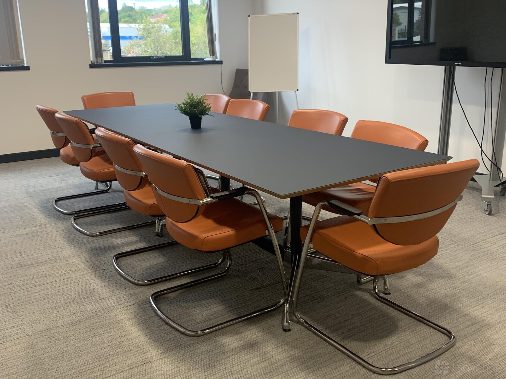 A meeting room with a long black table, orange chairs, and large windows at Lawrence House - Hub26.