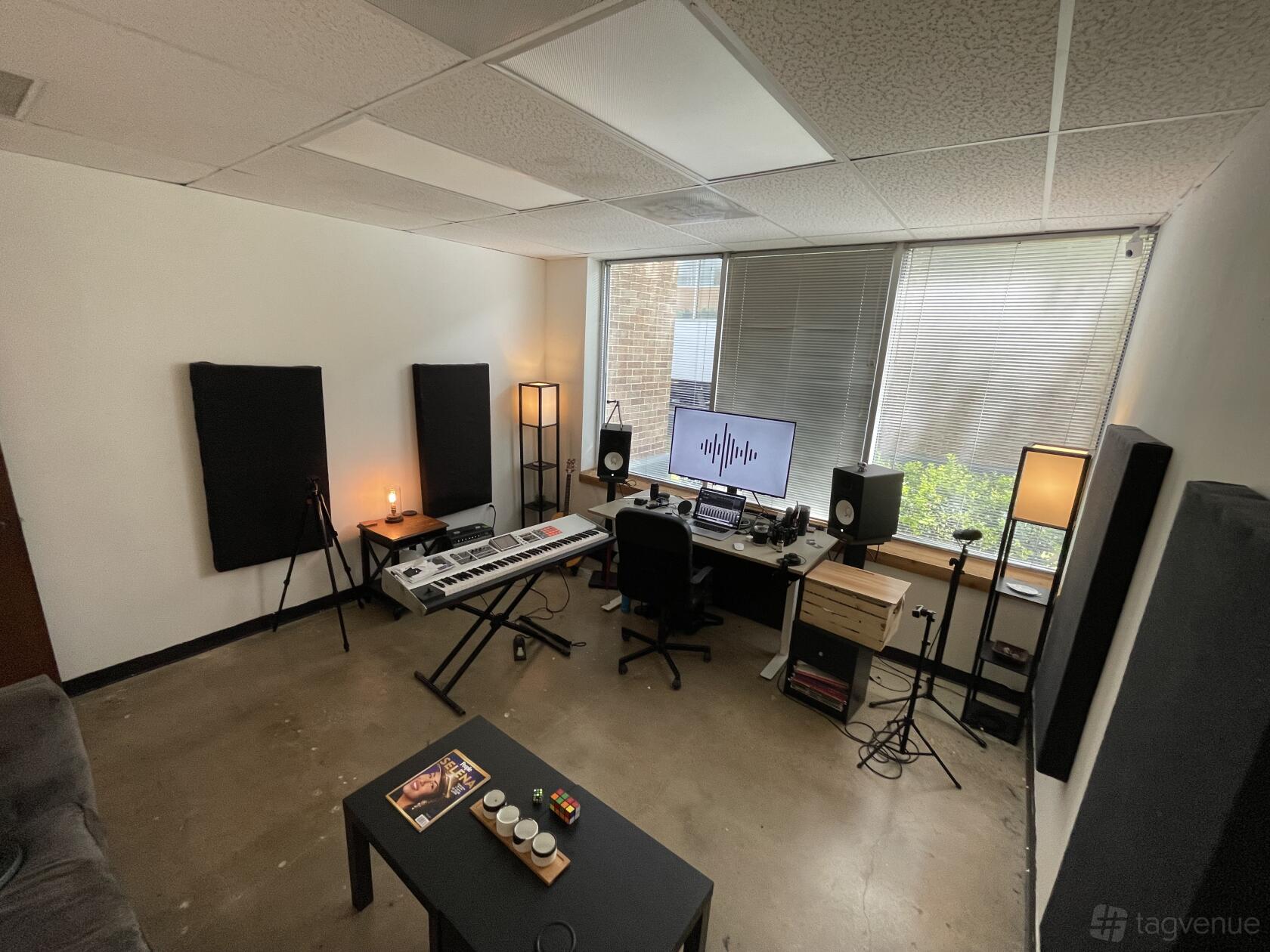 A music studio with a keyboard, soundproof panels, recording equipment, and large windows at The Creatives Factory.
