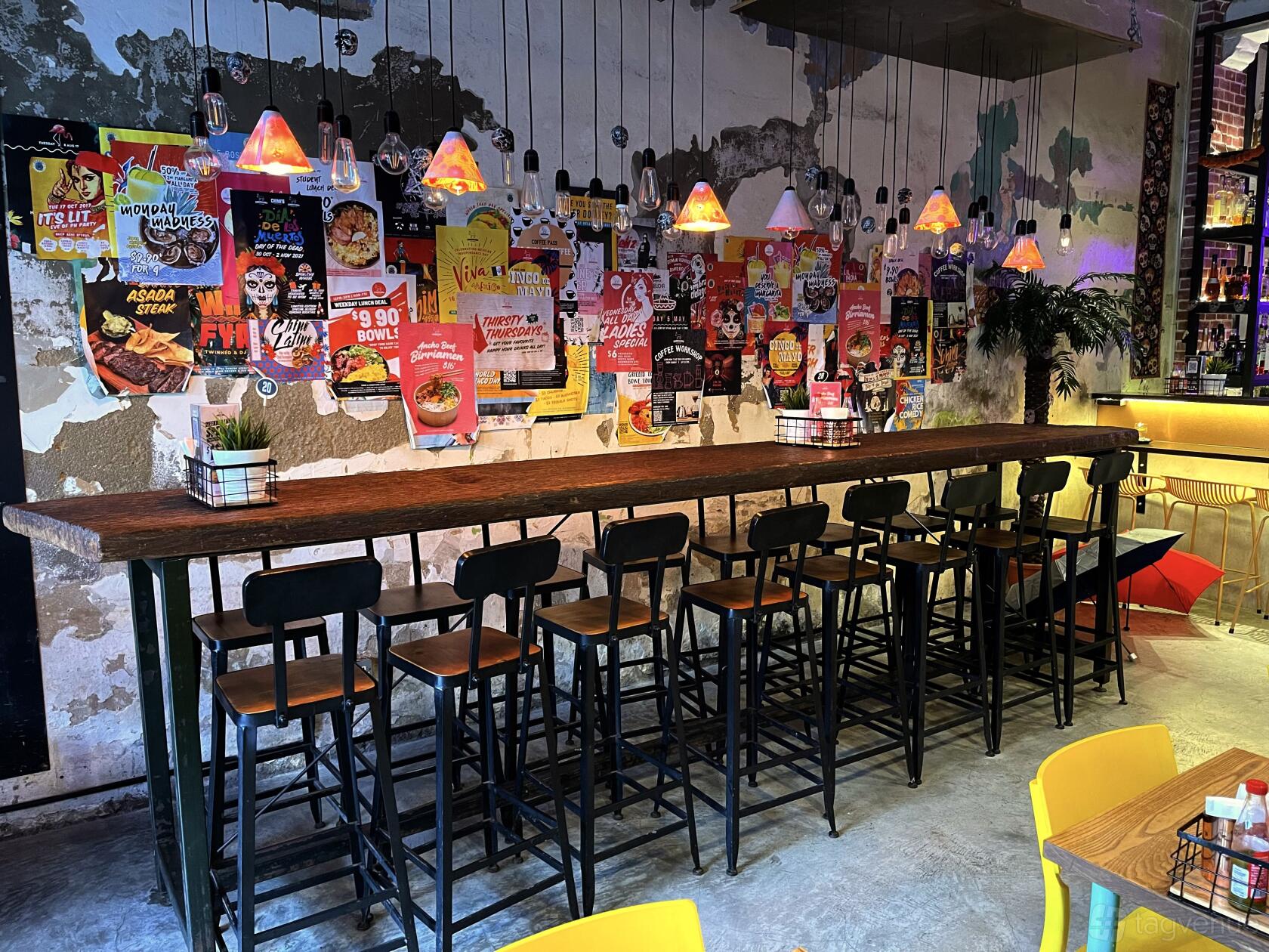 An event space in a bar featuring a long high wooden table with stools and colorful pendant lights at Chimichanga Dunlop.
