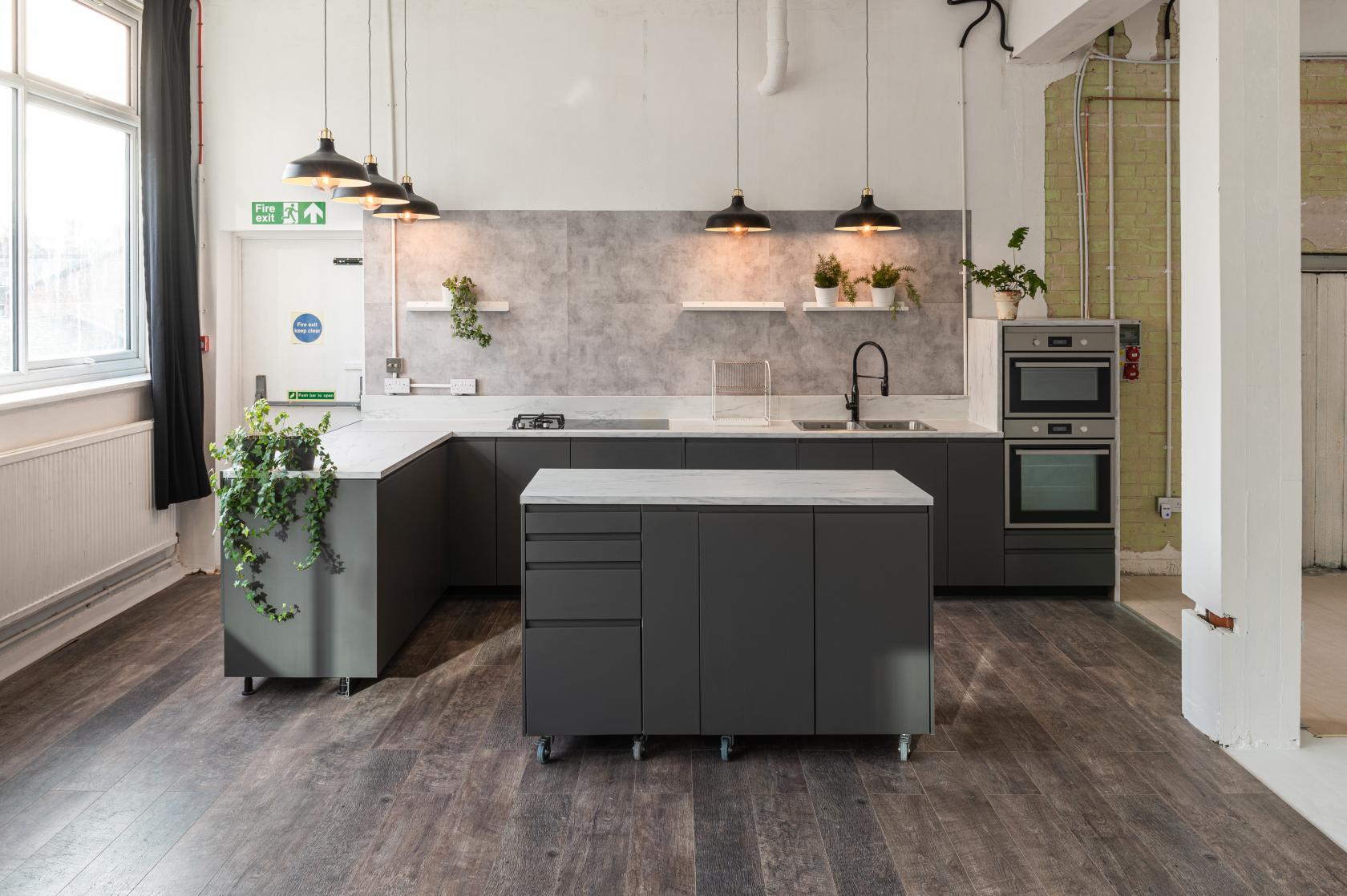 A studio kitchen with matte dark cabinetry, pendant lighting, marble countertops, and open shelves at 69 drops studios.