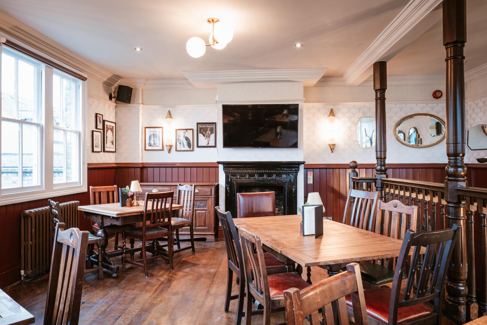 An event space in a pub with wooden floors, vintage chairs, a fireplace, and framed pictures at The George IV.