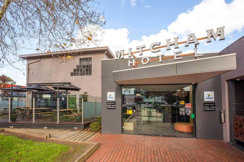 A pub entrance with glass doors, brick walkway, and outdoor seating with picnic tables at Mitcham Hotel.