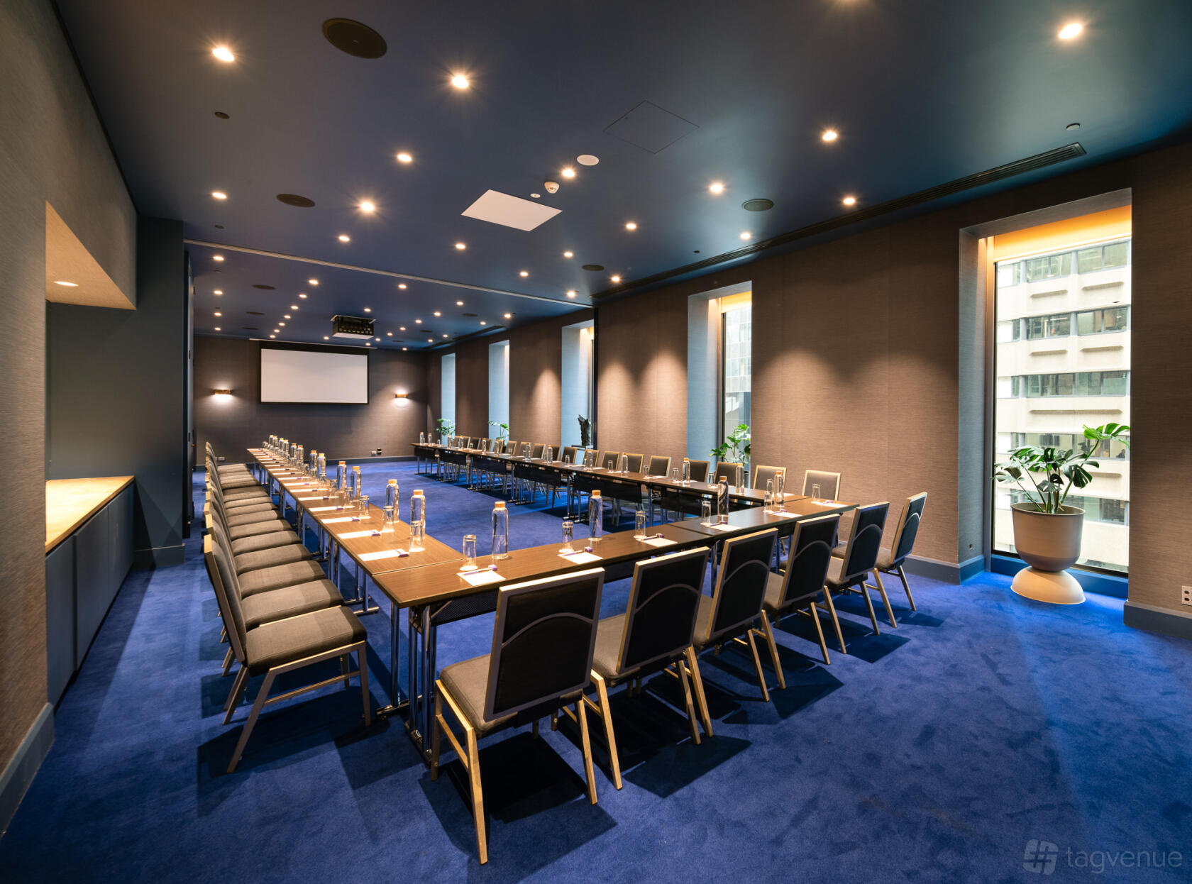 A meeting room with U-shaped table arrangement, blue carpet, bottled water, and large windows at Sofitel Sydney Wentworth.