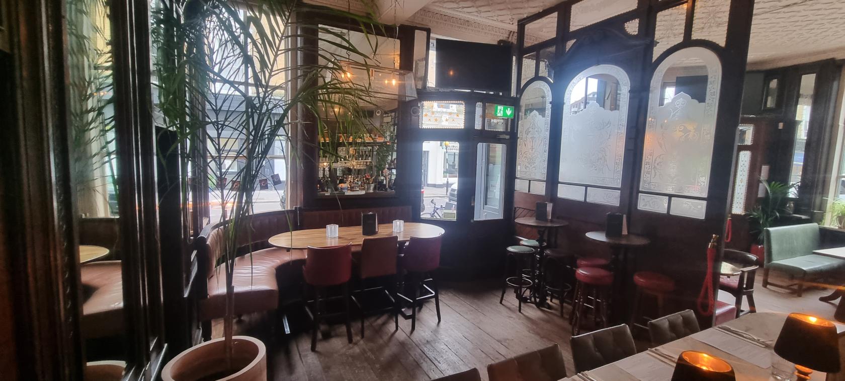 A pub room with etched glass partitions, wooden floors, round tables, and red upholstered chairs at The Washington.