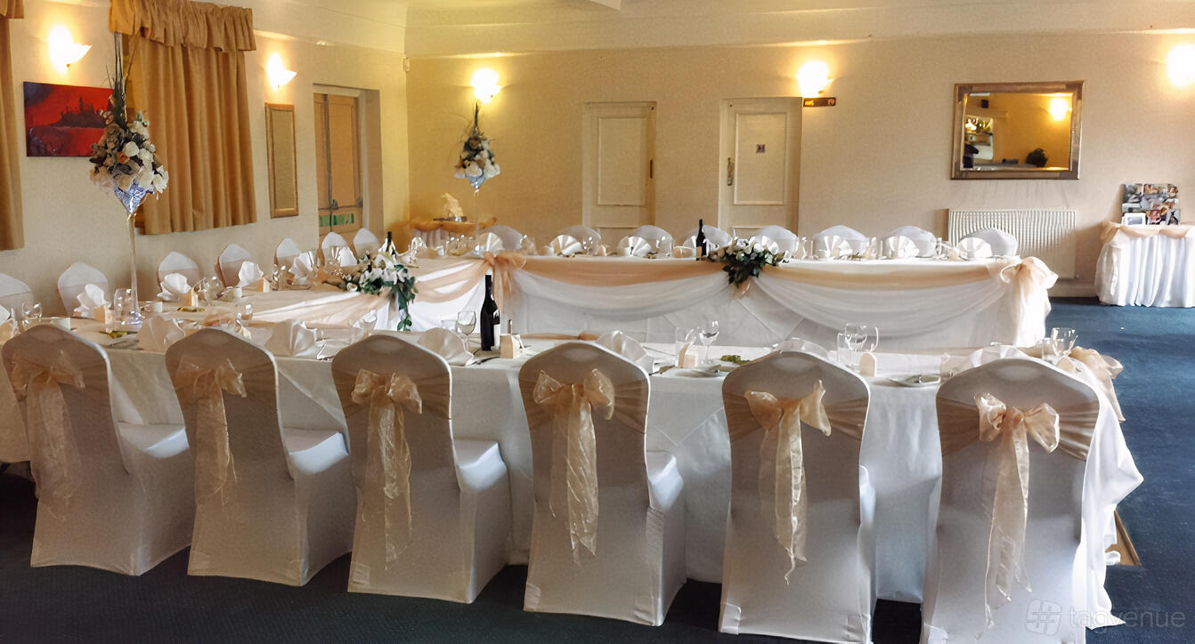 An event space with banquet tables, white chair covers with bows, and floral centerpieces at The Thurrock Hotel.