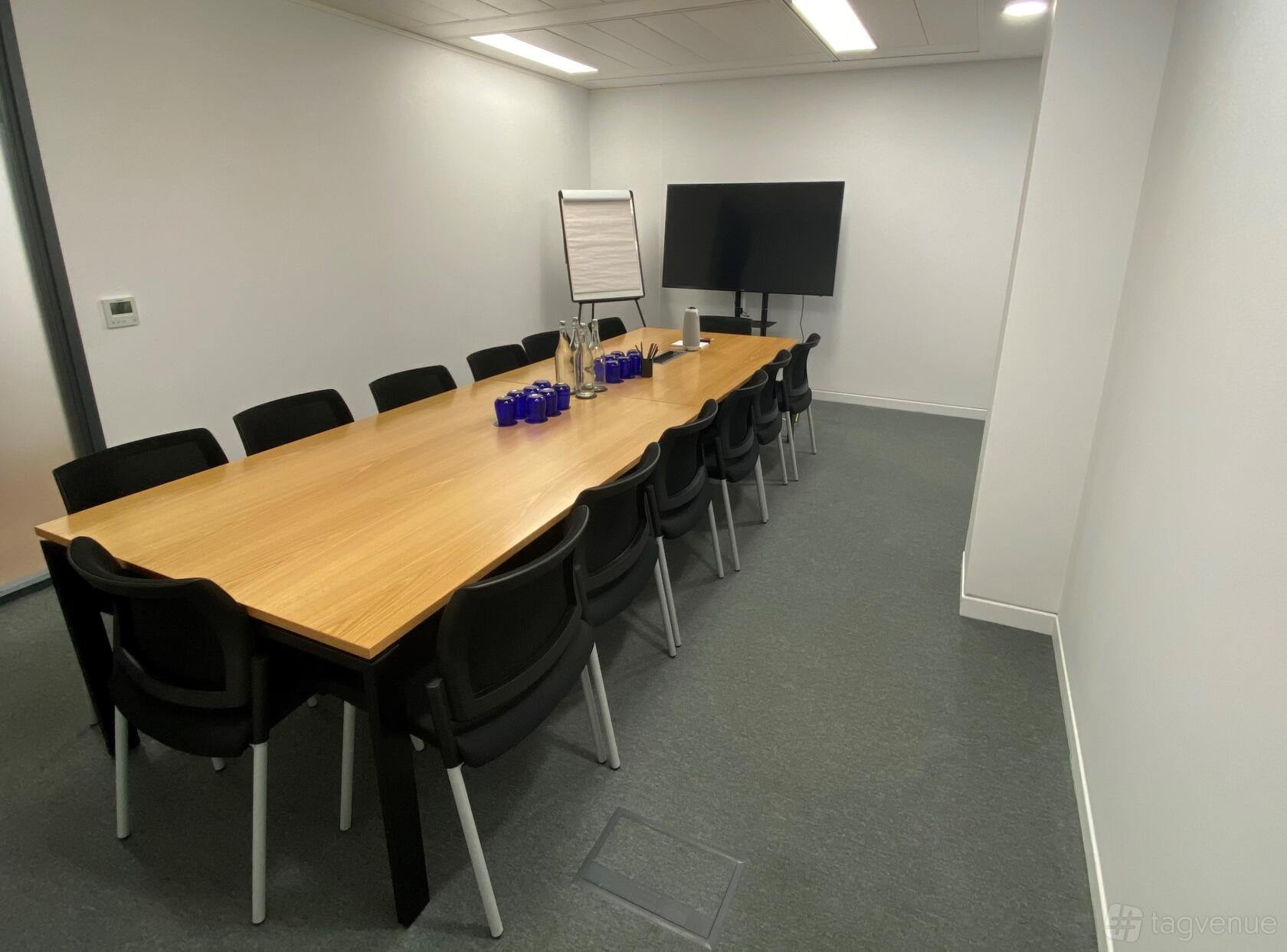 A meeting room with a long wooden table, black chairs, flipchart, and large TV screen at Landmark: New Cavendish Street, London.