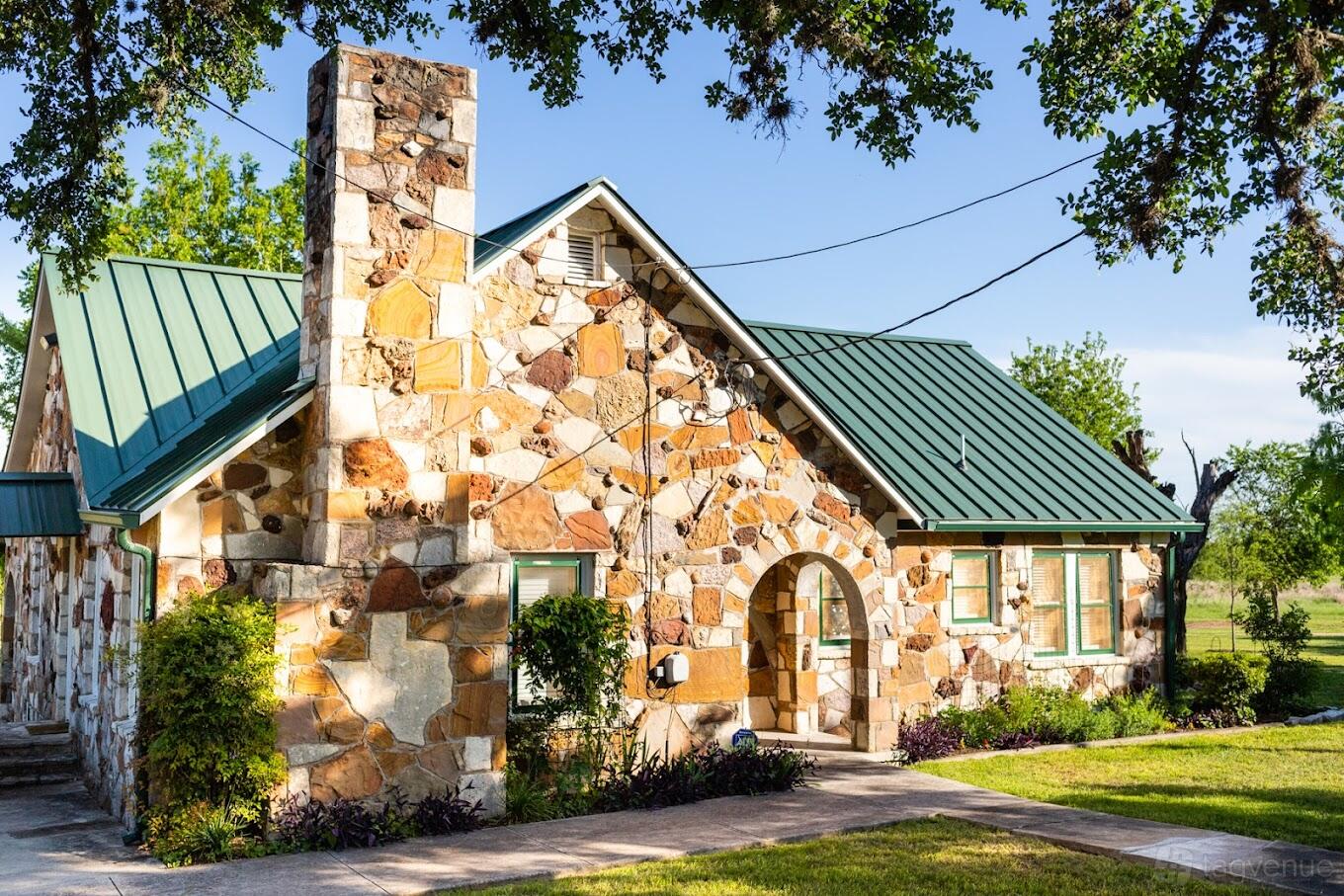 A rustic barn with a stone exterior, green metal roof, and arched entryway at Texas Rock House.