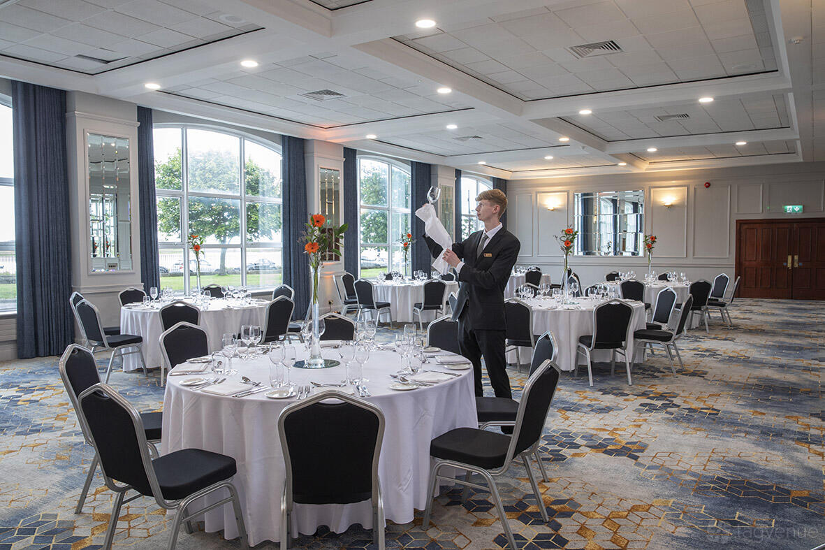 An event space with round tables, white linens, large windows, and floral centerpieces at Grand Hotel.