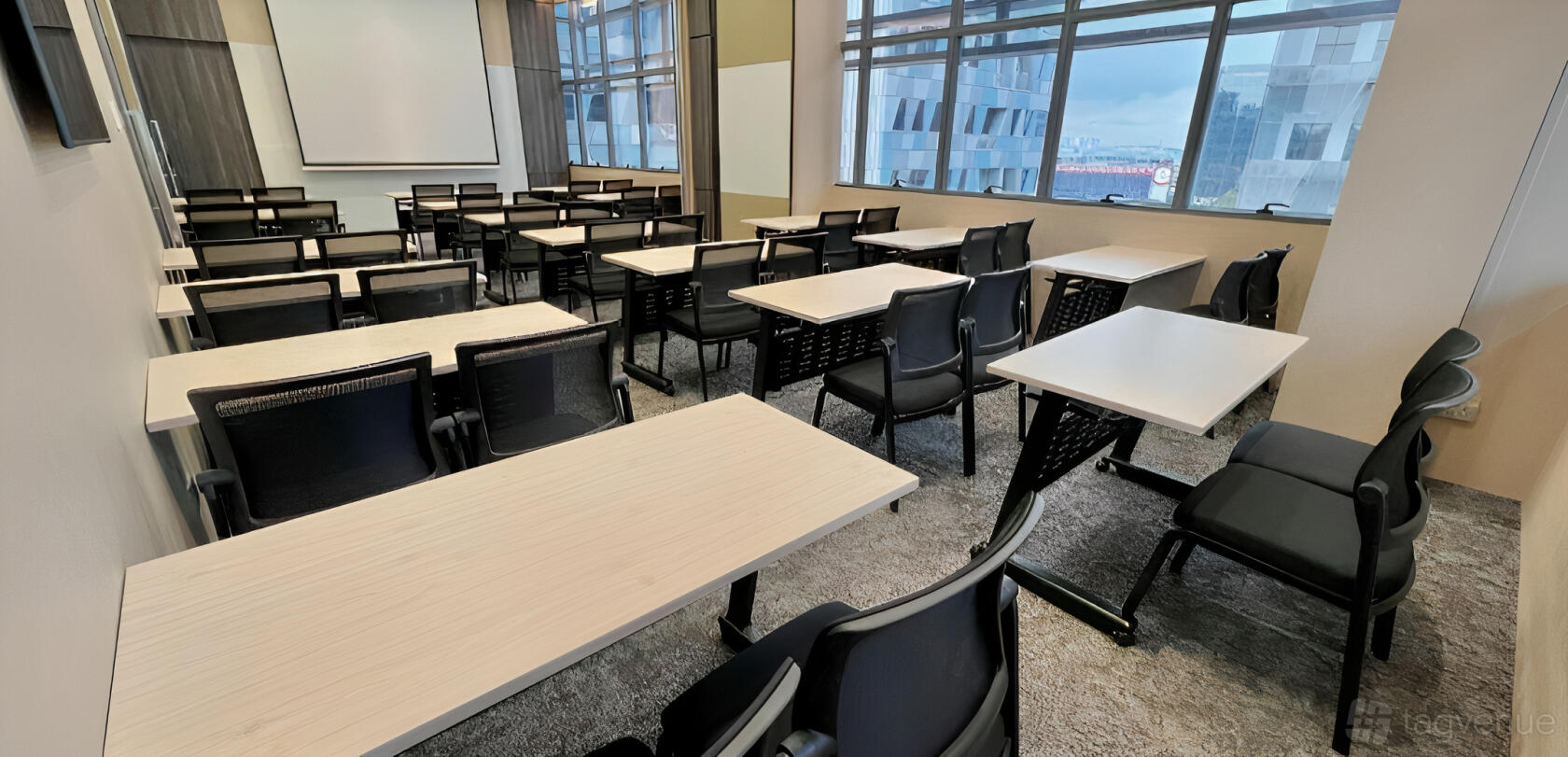 A meeting room with rows of rectangular tables, black chairs, a projector screen, and large windows at Fine Wines SG.