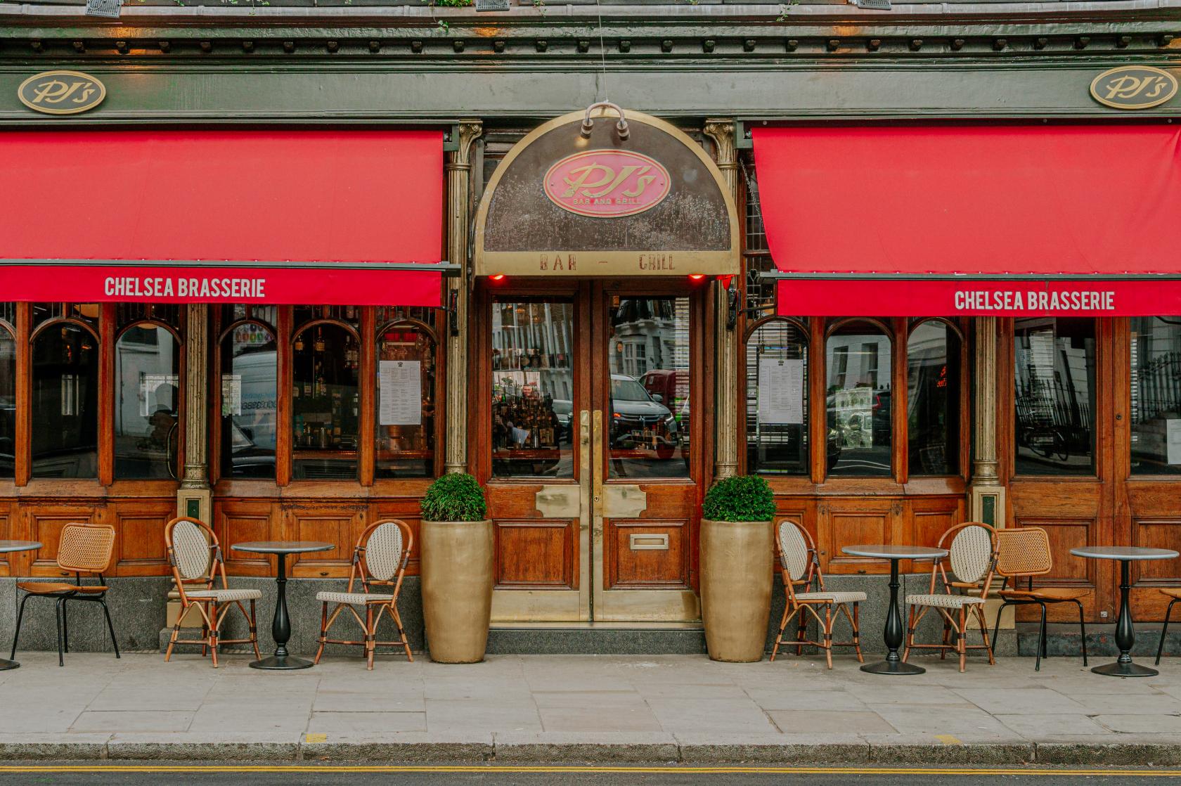 A restaurant with red awnings, outdoor café tables, wicker chairs, and wood-framed windows at PJ's Chelsea Brasserie.