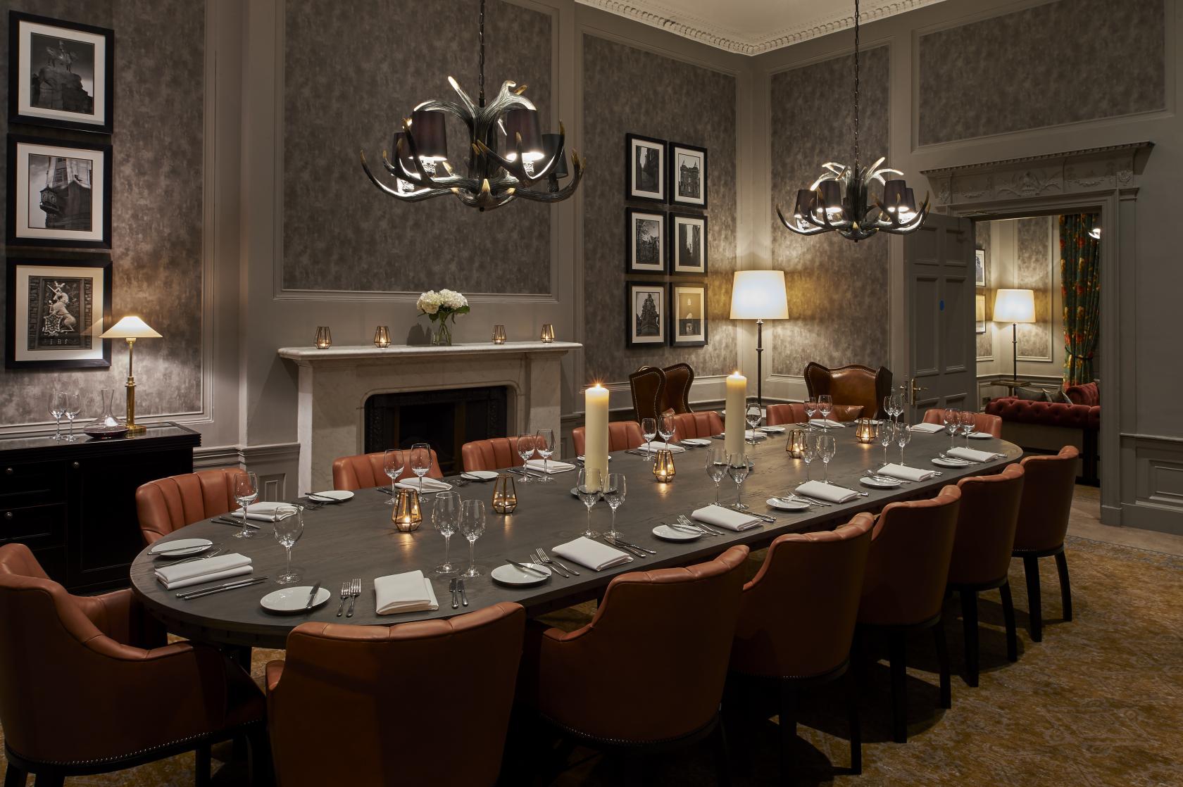 A hotel dining room with a long wooden table, orange leather chairs, antler chandeliers, and candlelight at Kimpton Charlotte Square Edinburgh.