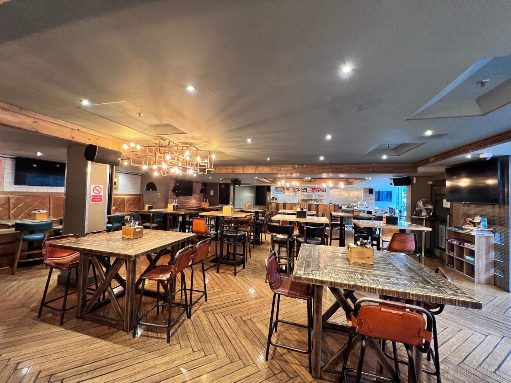 A restaurant with wooden tables, leather chairs, a geometric chandelier, and herringbone wood flooring at Tank and Paddle Bishopsgate.
