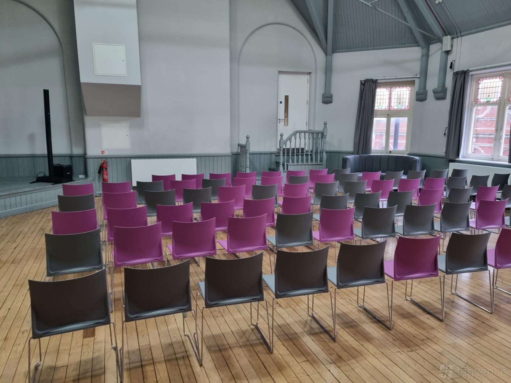 A hall with rows of purple and gray chairs, hardwood floors, and arched windows at Unity Hall and Business Space.