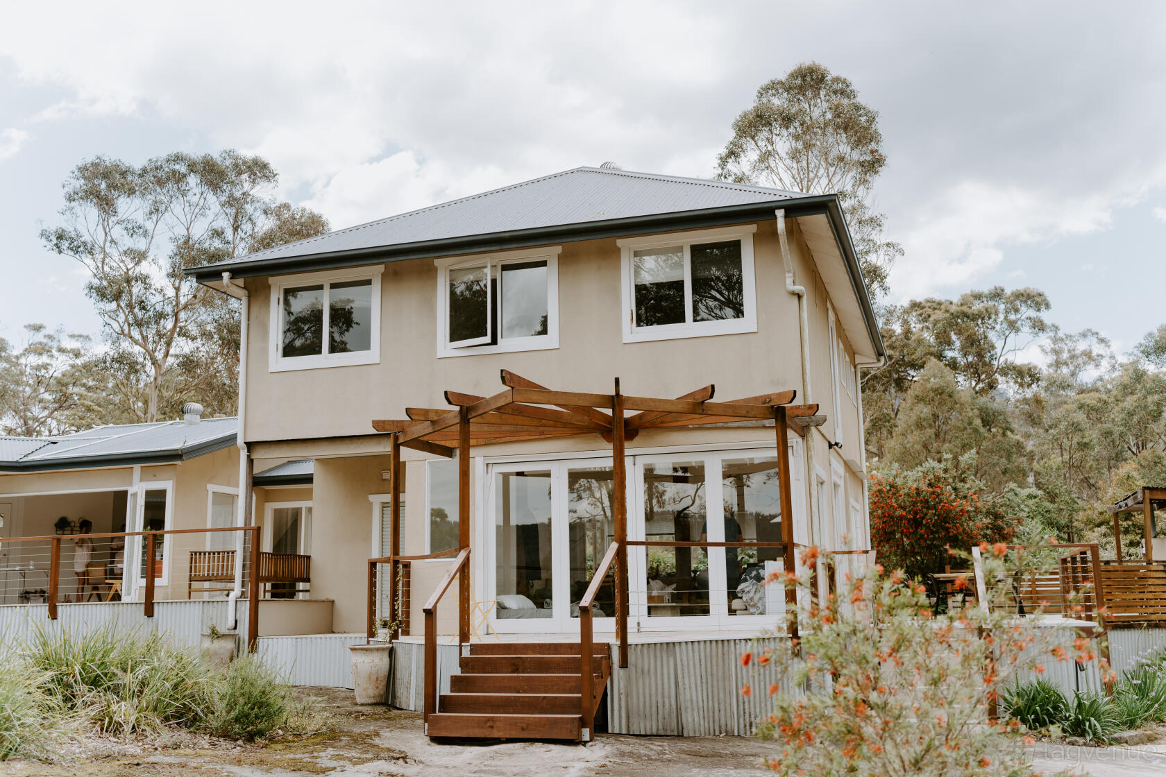 An open air venue with a two-story building, pergola-covered patio, and surrounding native trees at Wildwood Kangaroo Valley.