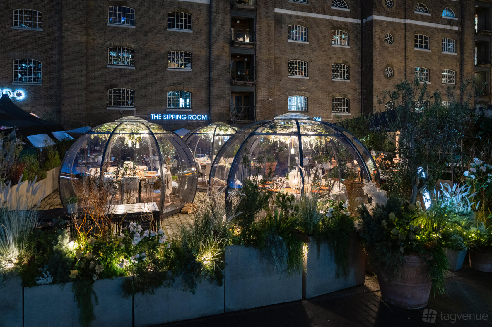 Outdoor dining room with glass igloos surrounded by greenery and illuminated string lights at The Sipping Room.