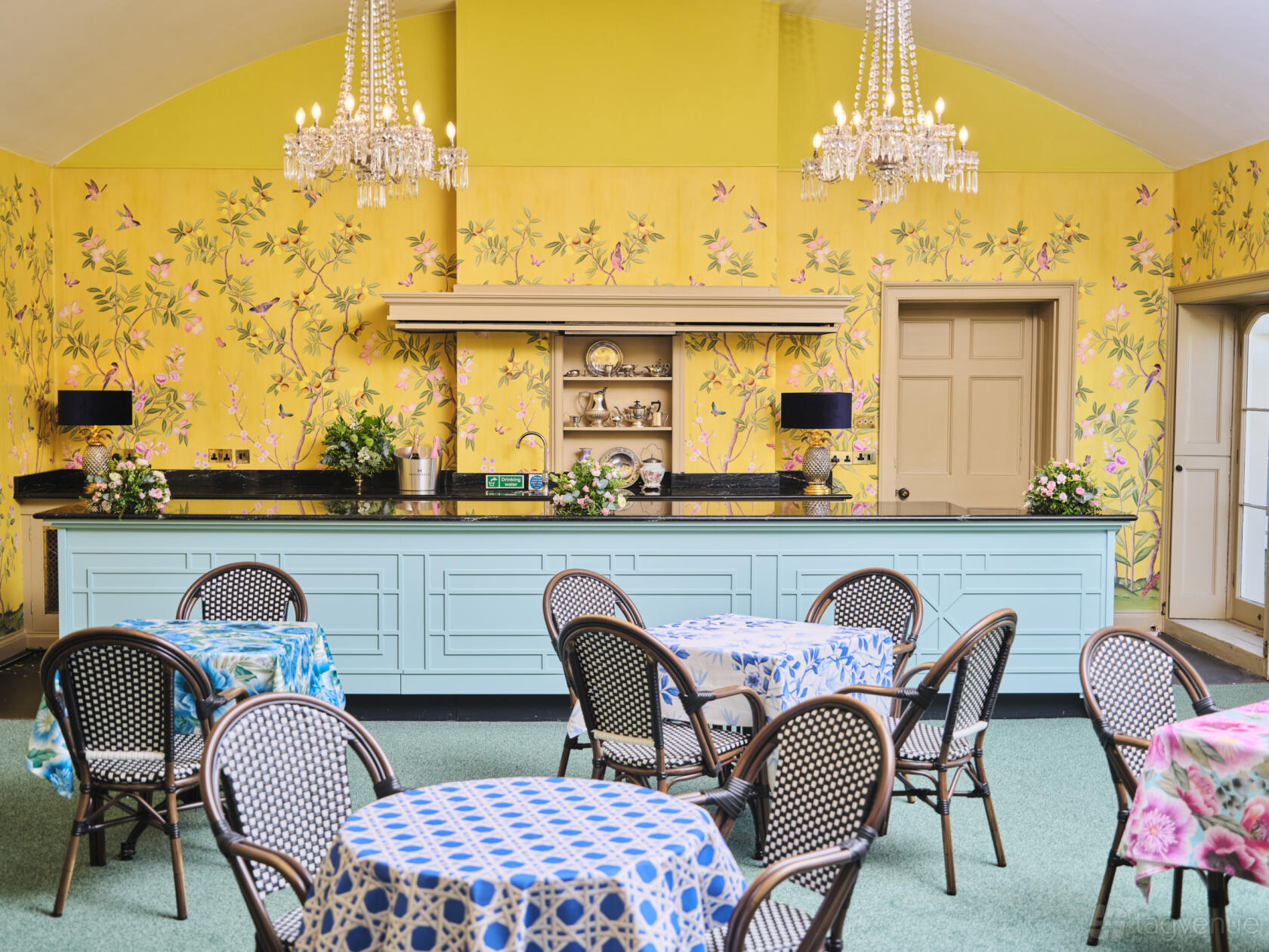 An event space in a museum with patterned wallpaper, chandeliers, and round tables with floral linens at Royal Pavilion.