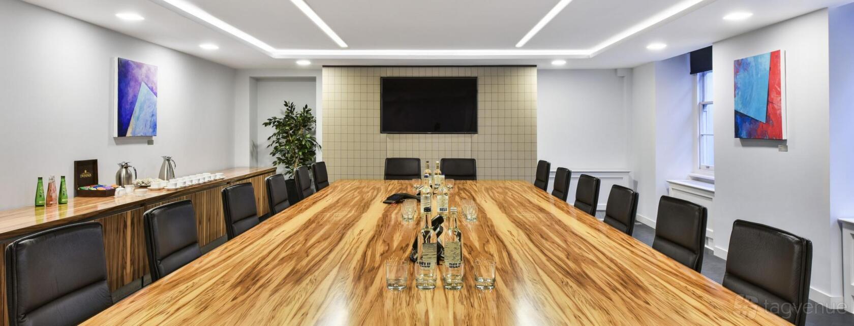 A meeting room with a large wooden conference table, bottled water, black chairs, and a wall-mounted TV at 8-10 Hill Street.