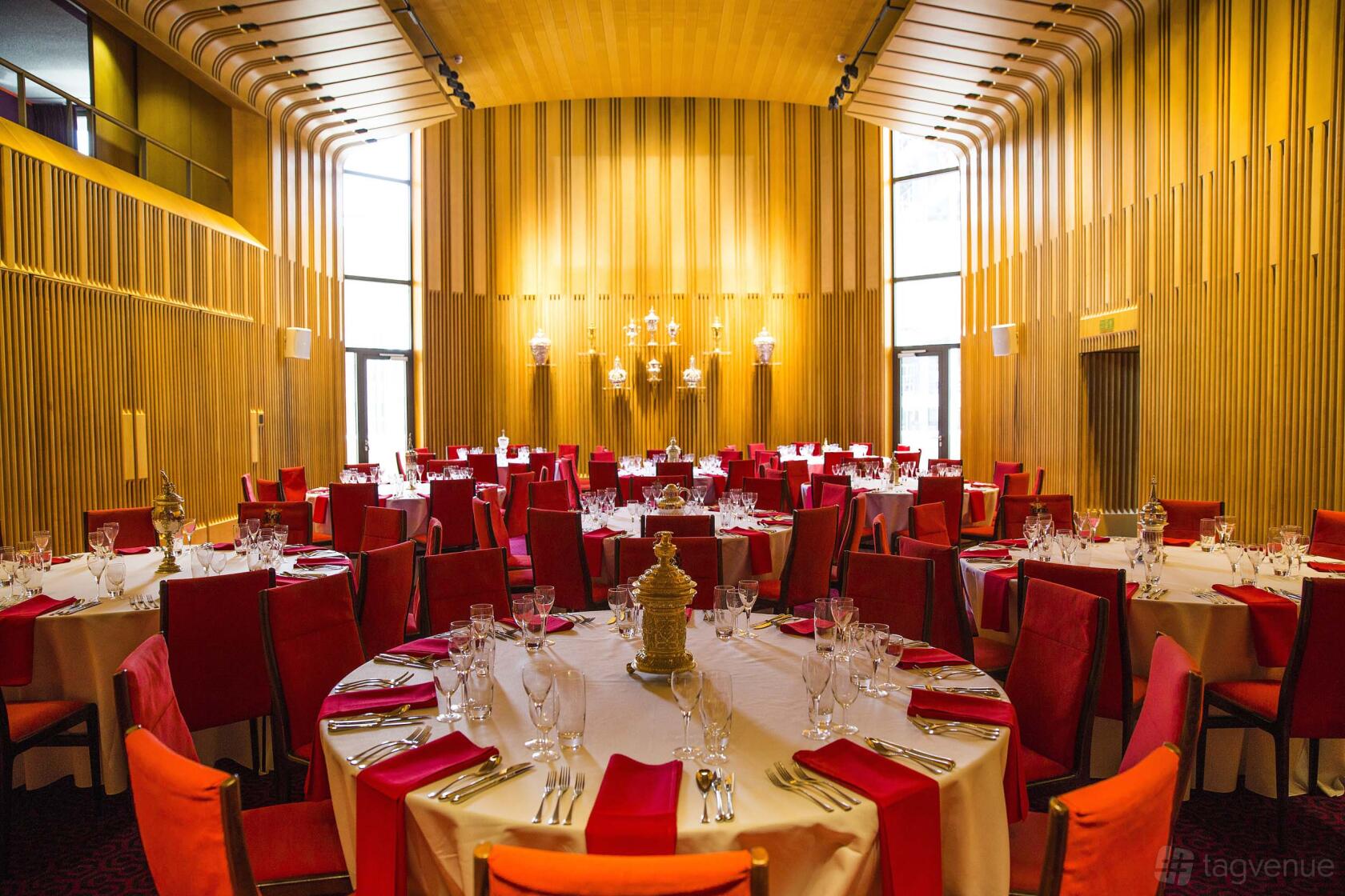 A hall with high wood-paneled walls, large windows, and round tables set with red chairs at Salters’ Hall.