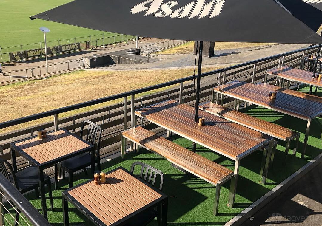 An outdoor cafe terrace with wooden tables, bench seating, and large umbrellas at The Last Piece Restaurant.