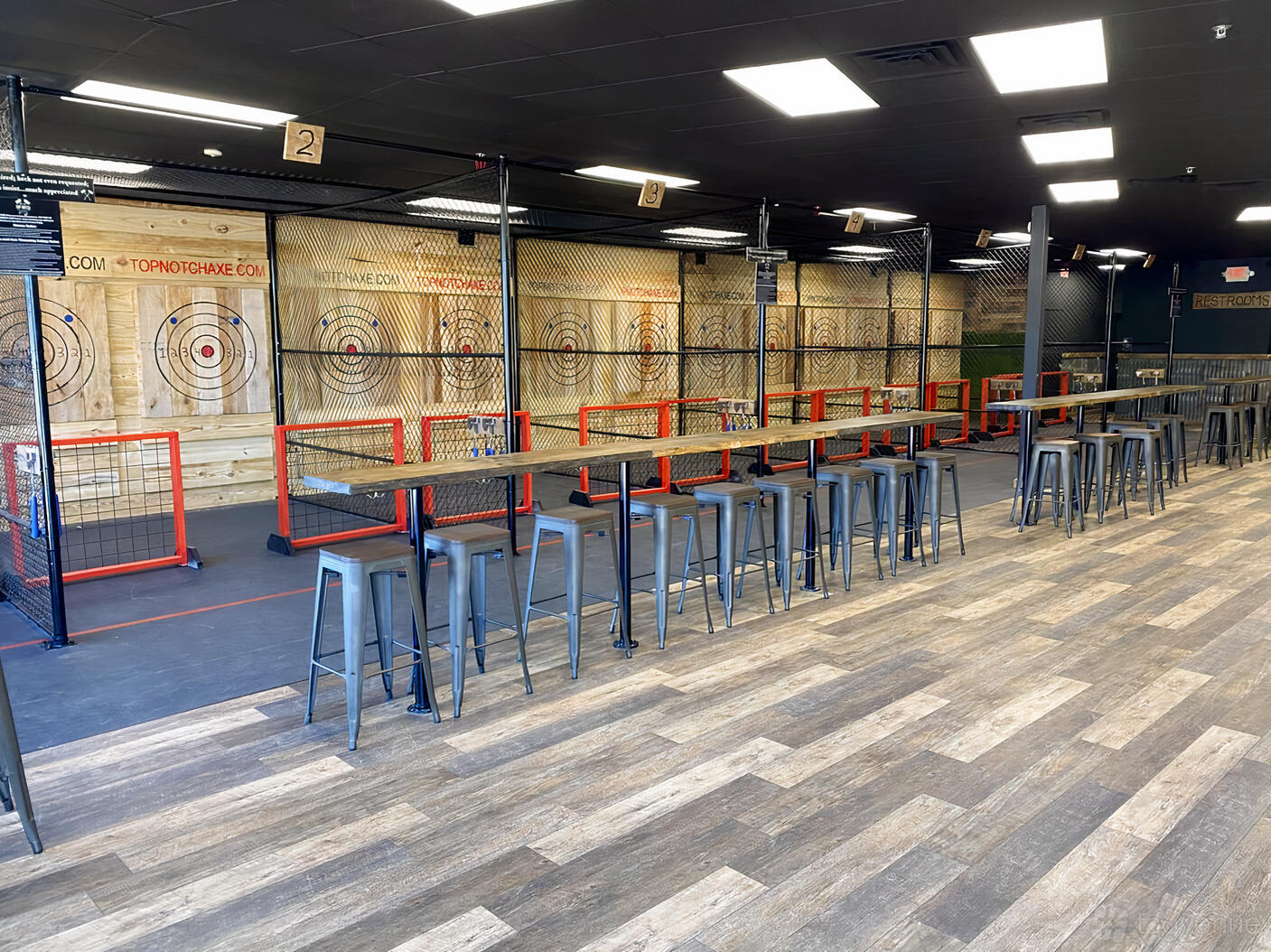 A sports club with multiple axe throwing lanes, tall tables, and metal stools at Top Notch Axe Throwing Round Rock.