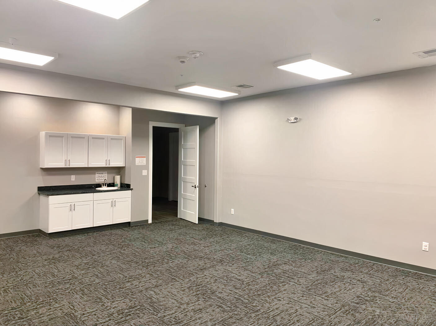 A classroom with gray carpet, white walls, ceiling lights, and built-in cabinets at Manvel Mansion Event Center.