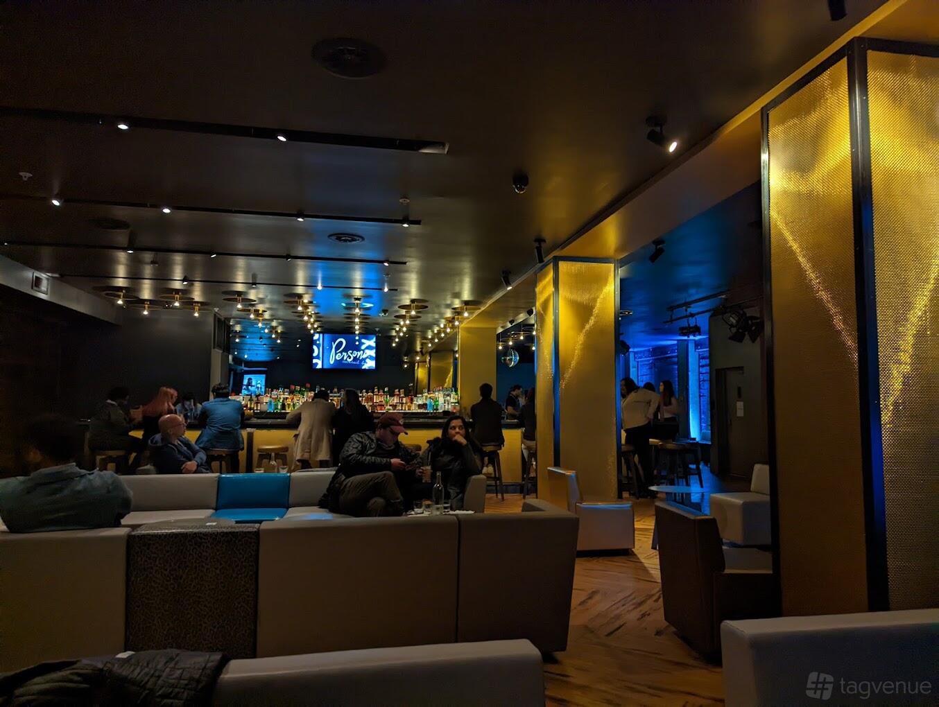 A function room in a cocktail bar with ambient lighting, plush seating, and a backlit bar at Persona.