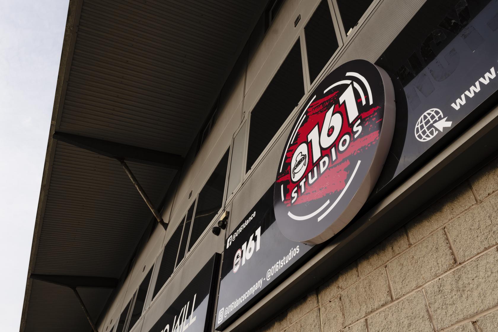 An exterior view of a dance studio with branded signage and large windows at 0161 Studios.