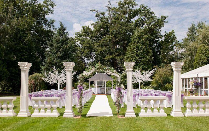 An outdoor event space with white pillars, a central aisle, and a gazebo surrounded by decorated chairs at Trunkwell House Hotel.