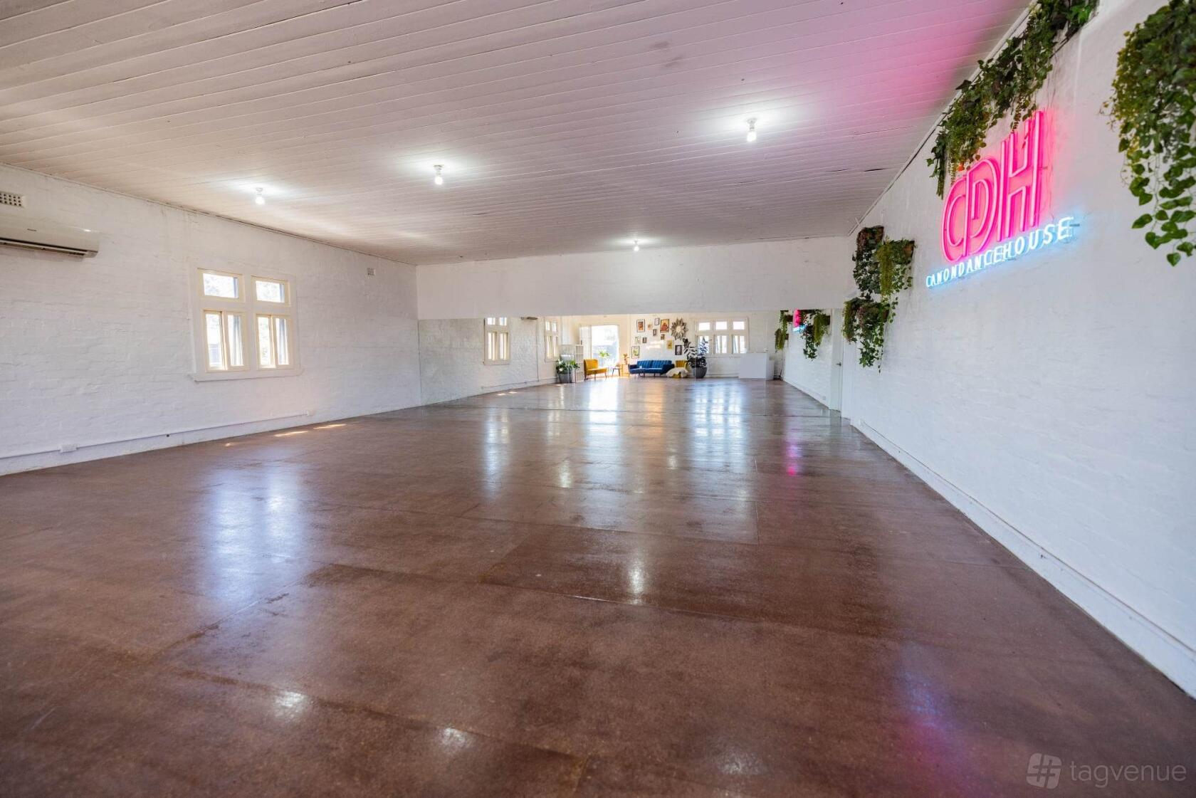 A dance studio with polished floors, white brick walls, and a neon Canon Dance House sign at Canon Dance House.