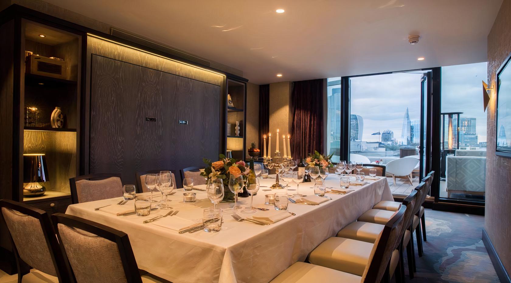 A private dining room with a large set table, floor-to-ceiling windows, and skyline views at Aviary Rooftop Bar & Restaurant.